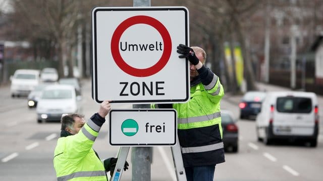 Zwei Arbeiter befestigen ein Hinweis-Schild für eine Umweltzone. Zwei Arbeiter befestigen ein Hinweis-Schild für eine Umweltzone.