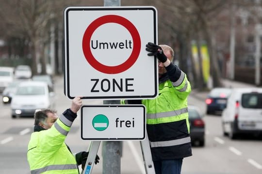 Zwei Arbeiter befestigen ein Hinweis-Schild für eine Umweltzone.