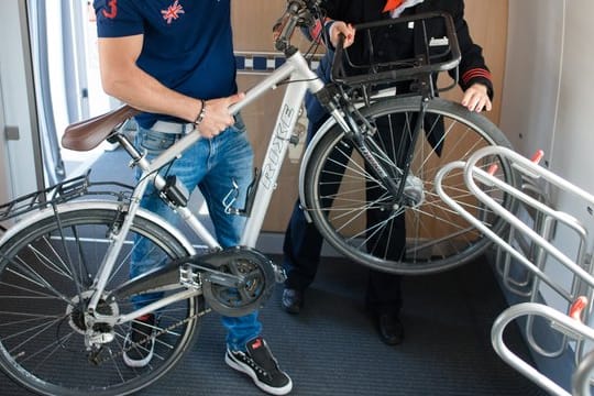 Ein Fahrgast verstaut sein Fahrrad in einem ICE 4, während ihm eine Zugführerin dabei hilft.