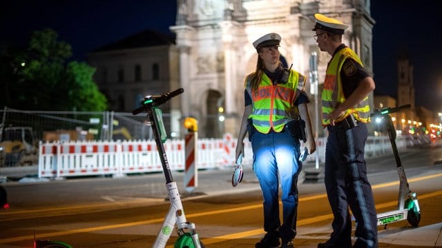 Polizisten stehen bei einer E-Tretroller-Kontrolle an der Straße.