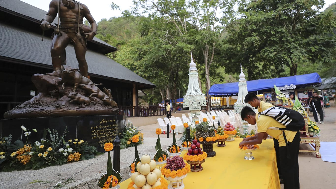 Einige der geretteten Jugendlich beten vor einer Statue des bei der Rettung gestorbenen Tauchers: In der Höhle sollen Geräte ausgestellt werden, die bei der Bergung zum Einsatz kamen.