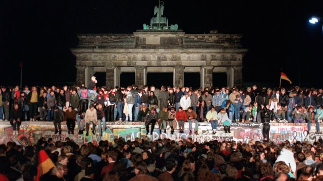 Jubelnde Menschen sitzen nach der Maueröffnung auf den Grenzanlagen am Brandenburger Tor.