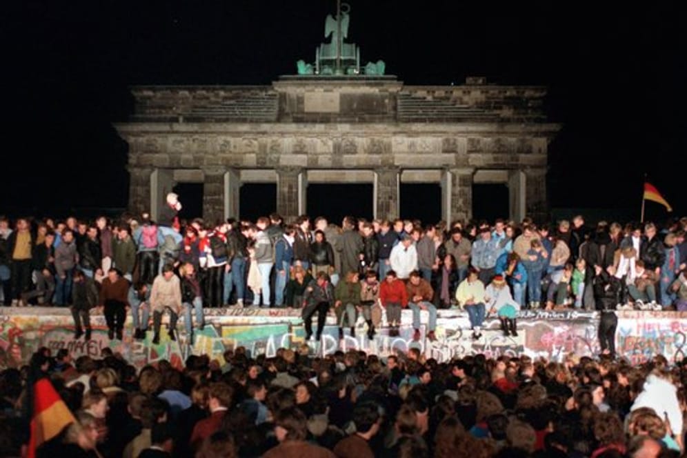 Jubelnde Menschen sitzen nach der Maueröffnung auf den Grenzanlagen am Brandenburger Tor.