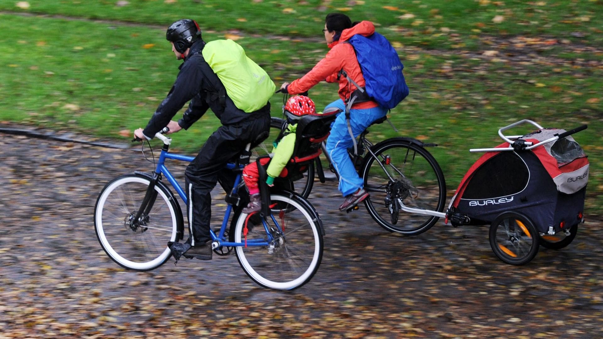 Eine Familie radelt mit Kindersitz und Kinderanhänger durch den Park: Welche Sitzposition ist sicherer?