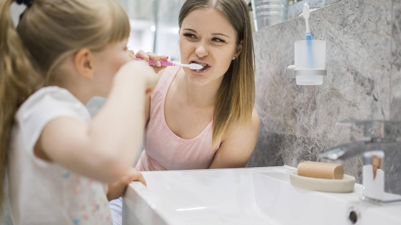 Mutter und Tochter putzen sich die Zähne: Gerade bei Kindern wird eine höher dosierte Zahnpasta mit Fluorid empfohlen.