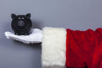 Weihnachtsmann hält Sparschwein auf der Hand: Die Höhe des Weihnachtsgeldes variiert zwischen den Branchen stark.