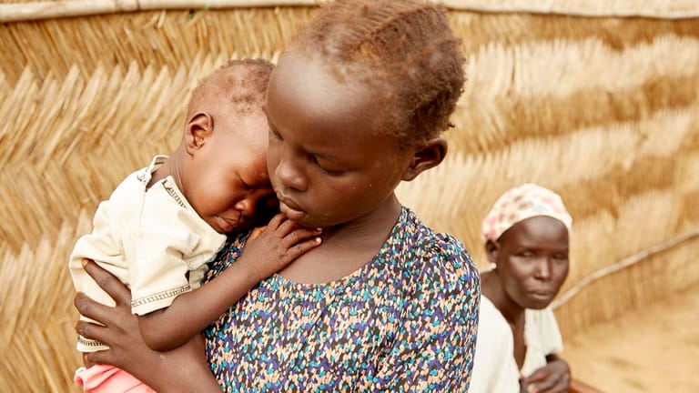 Adut (14 Monate) aus dem Südsudan auf dem Arm ihrer großen Schwester Lydia. Adut ist lebensbedrohlich mangelernährt.