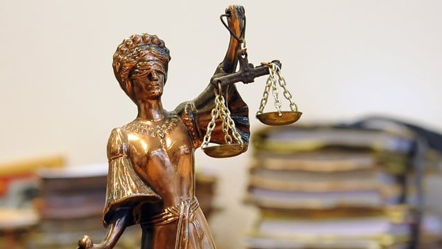 Eine goldfarbene Justitia-Figur steht vor Aktenbergen