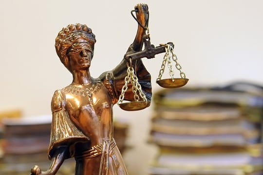 Eine goldfarbene Justitia-Figur steht vor Aktenbergen