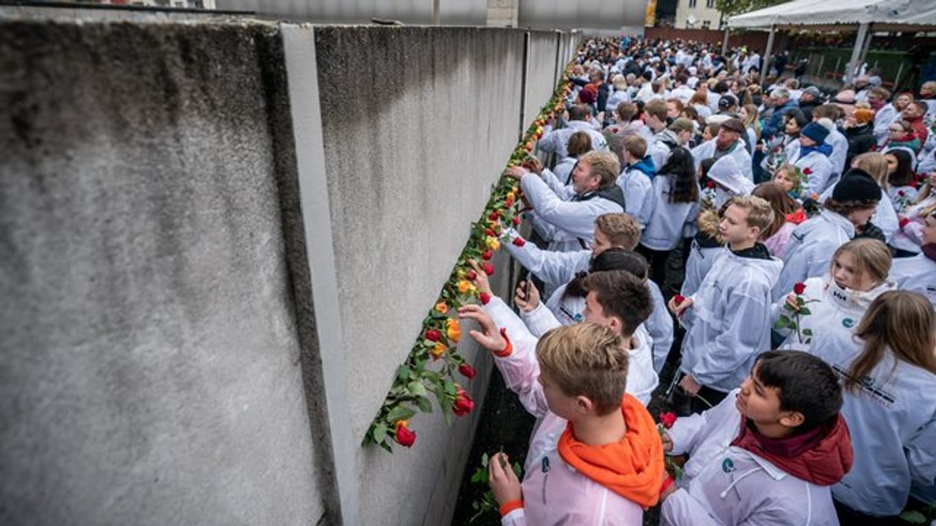 Besucher stecken Blumen bei der Gedenkveranstaltung der Stiftung Berliner Mauer an der Bernauer Straße in Mauerschlitze der Hinterlandmauer.