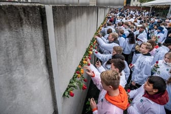 Besucher stecken Blumen bei der Gedenkveranstaltung der Stiftung Berliner Mauer an der Bernauer Straße in Mauerschlitze der Hinterlandmauer.
