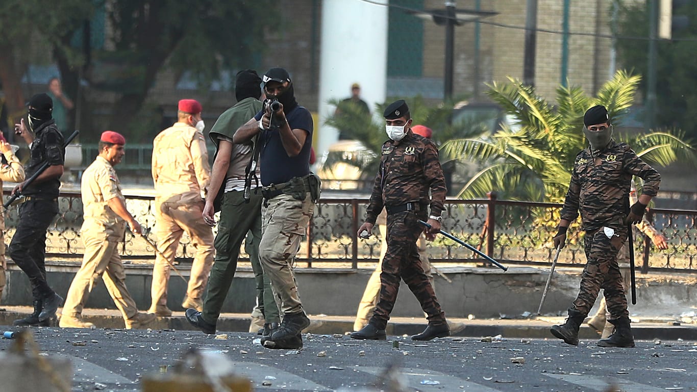 Ein vermummtes Mitglied der irakischen Sicherheitskräfte zielt mit einem Tränengasgewehr in die Menge der Demonstranten.