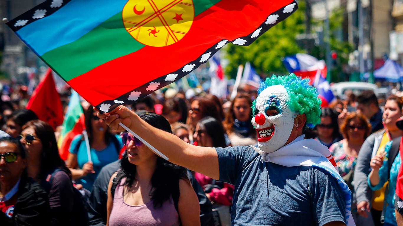 Ein Mann in Chile schwenkt die Flagge der indigenen Gemeinde der Mapuche: Auch hier wurden die Clownsmasken auf Protesten für Sozialreformen getragen.