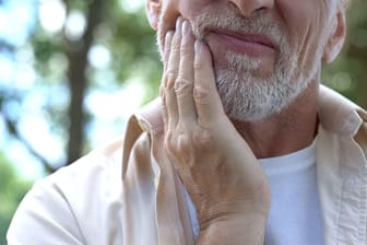 Ein Mann fasst sich an die Wange: Kieferschmerzen sind ein erstes Anzeichen für eine craniomandibuläre Dysfunktion.