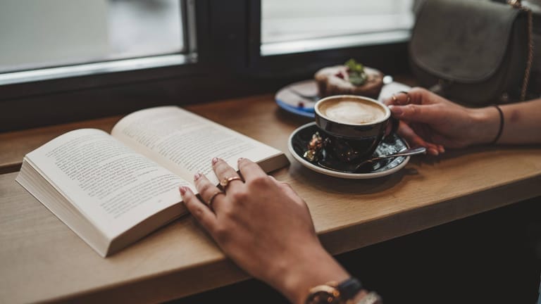 Eine Frau trinkt Kaffee und liest ein Buch: In Büchercafés kann man dem tristen Alltag ganz entspannt entfliehen.