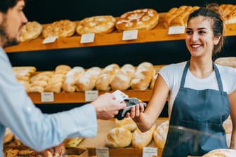 Kunde zahlt mit Karte in einer Bäckerei: Unternehmen mit elektronischen Kassensystemen sind ab 2020 verpflichtet, Kassenzettel auszudrucken.