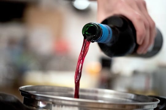 Mann kocht mit Rotwein: Theoretisch verdampft Alkohol beim Kochen – wie lang das dauert und ob wirklich alles verdampft, ist aber unklar.