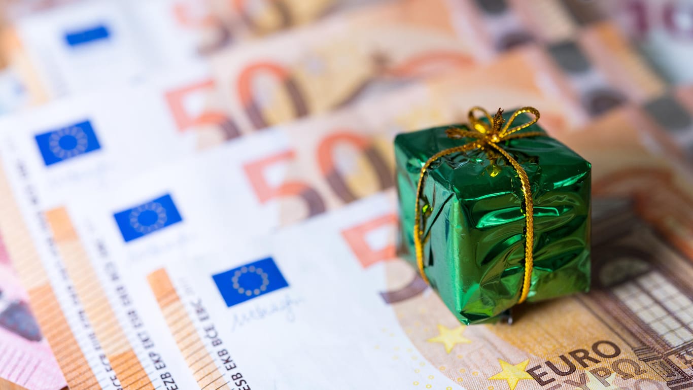 Ein kleines Geschenk liegt auf Banknoten: Die Chance auf Weihnachtsgeld ist in tarifgebundenen Unternehmen deutlich höher.