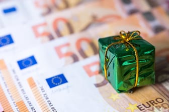 Ein kleines Geschenk liegt auf Banknoten: Die Chance auf Weihnachtsgeld ist in tarifgebundenen Unternehmen deutlich höher.