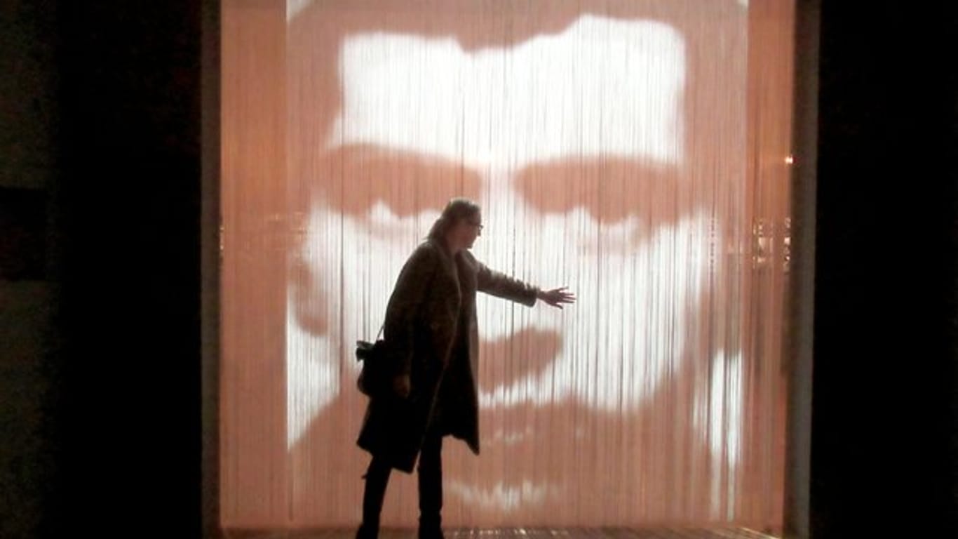 Eine Besucherin steht vor einem Kunstwerk, einem Streifenvorhang mit einem Porträt des französischen Konzeptkünstler Christian Boltanski.