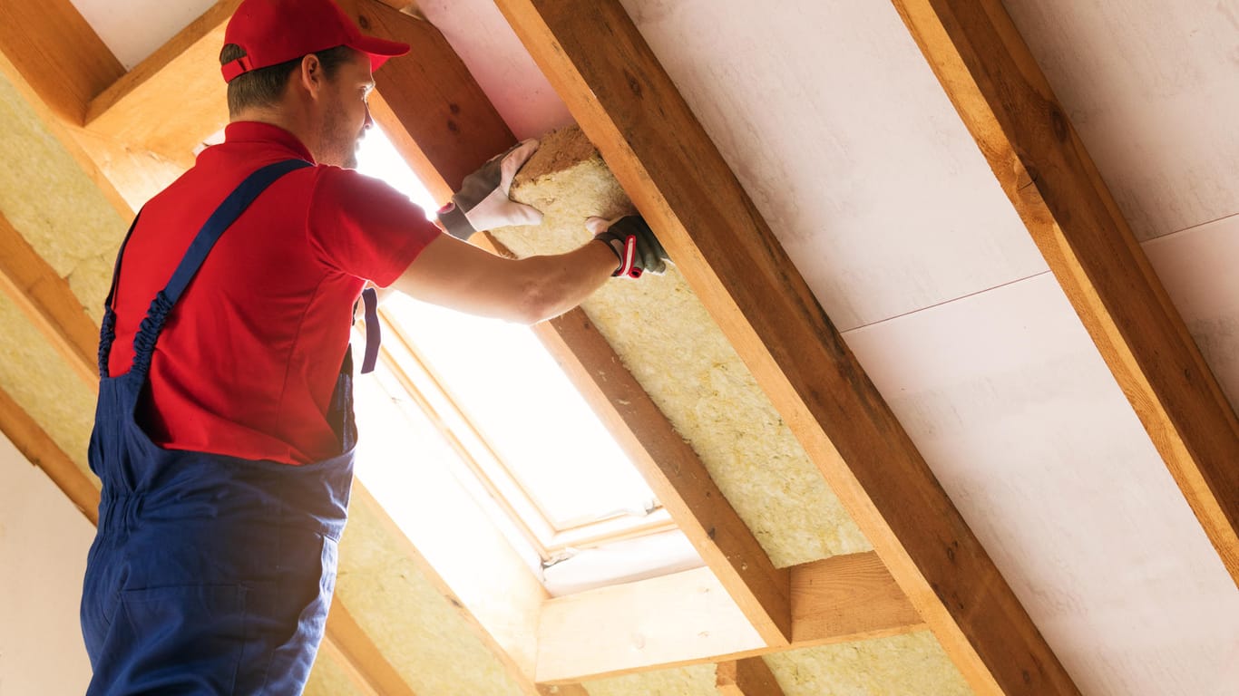 Ein Mann dämmt das Dach: Die richtige Wärmedämmung kann helfen, Energiekosten einzusparen.