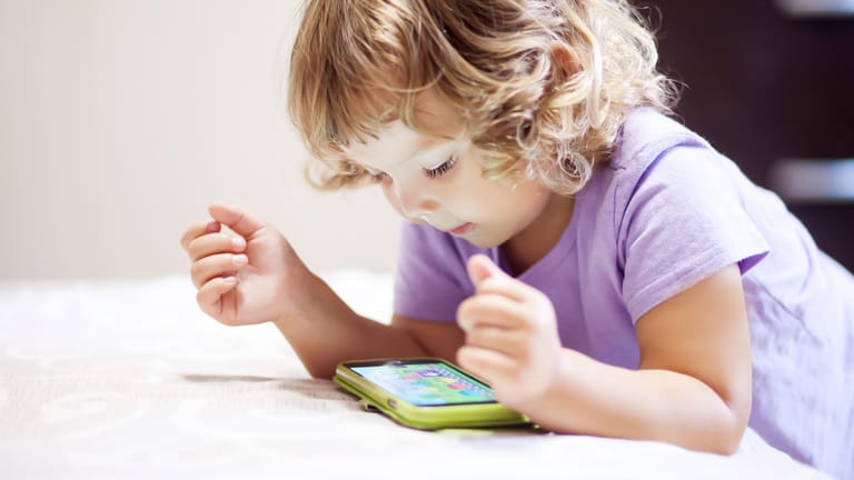 Ein Kleinkind schaut auf ein Handydisplay: Wie stark beeinträchtigt zu viel Zeit vor einem Bildschirm die Entwicklung des Kindes?