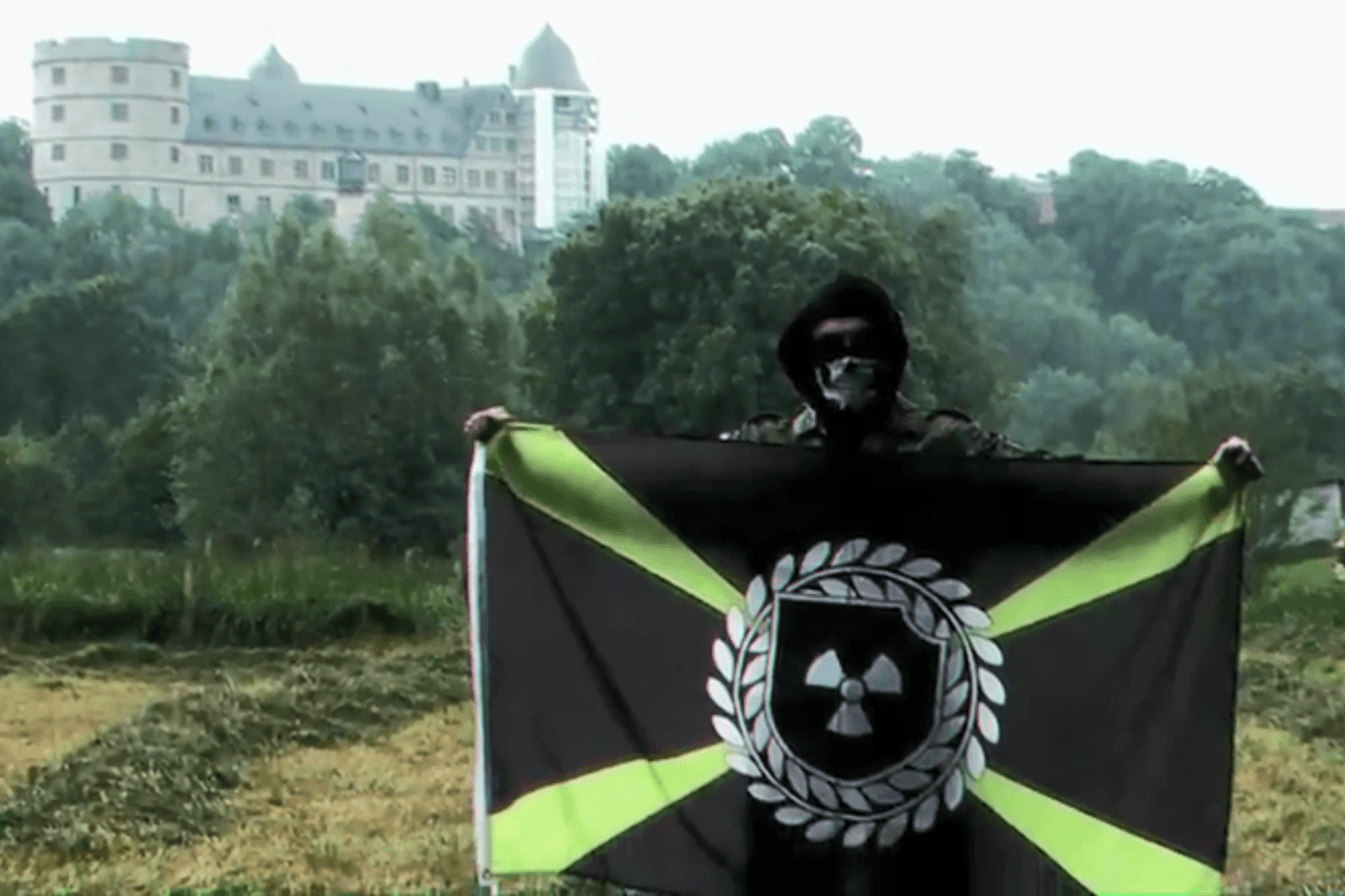 "Atomwaffen Division": Ein Neonazi mit der Flagge der Organisation steht im einzigen Video der deutschen Organisation vor der Wewelsburg. Ein Datenleck gibt Hinweise zu einem möglichen Beteiligten aus Thüringen.