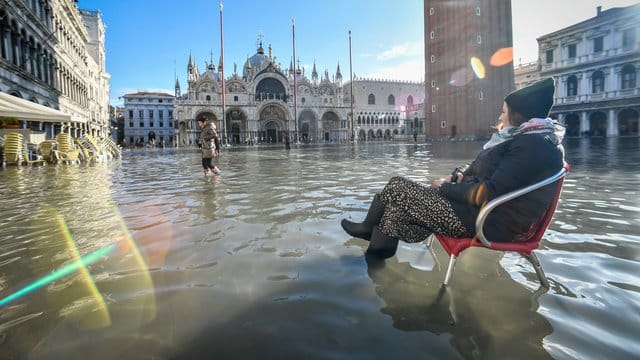 Eine Frau sitzt auf einem Stuhl im Hochwasser auf dem Markusplatz.