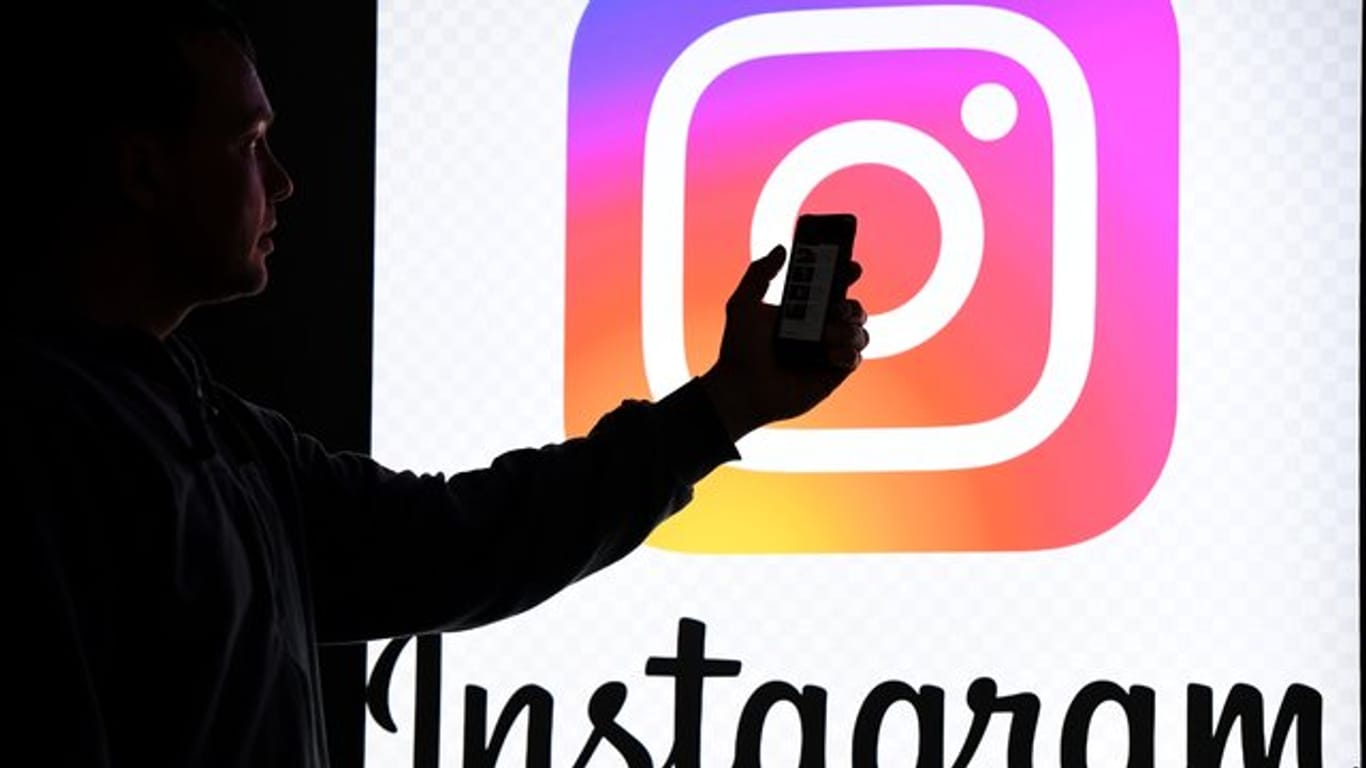 Ein Mann hält ein Smartphone vor einem Monitor mit dem Logo von Instagram.