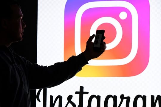 Ein Mann hält ein Smartphone vor einem Monitor mit dem Logo von Instagram.