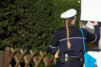 Eine Polizistin wirft eine Informationsbroschüre in einen Briefkaste: 800 Männer will die Polizei testen lassen.