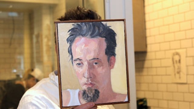 Sebastian Brecht hält sich ein Portrait vor sein Gesicht, das die Künstlerin Alix Bailey von ihm gemalt hat. Sebastian Brecht hält sich ein Portrait vor sein Gesicht, das die Künstlerin Alix Bailey von ihm gemalt hat.