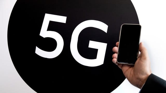 Ein Smartphone wird vor einen 5G-Schriftzug gehalten: Derzeit gehen die meisten Forscher nicht davon aus, dass Mobilfunk sich auf die Gesundheit auswirkt. Für Zeiträume von mehr als zehn Jahren reicht die Datenlage laut WHO aber noch nicht aus.