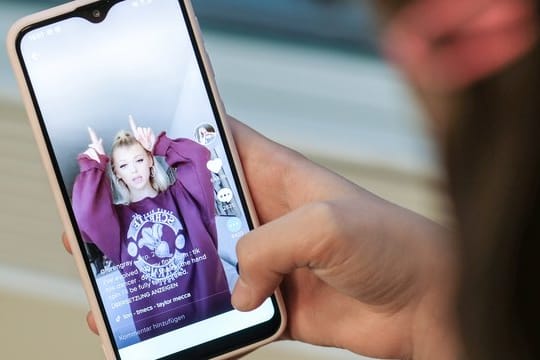 Ein Mädchen hält ihr Smartphone in den Händen, auf dem sie in der Kurzvideo-App TikTok das Profil von @lorengray geöffnet hat.