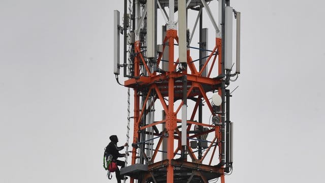 Ein Techniker klettert an einem Funkmast neben Mobilfunkantennen für den Mobilfunkstandard 5G. Ein Techniker klettert an einem Funkmast neben Mobilfunkantennen für den Mobilfunkstandard 5G.