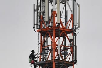 Ein Techniker klettert an einem Funkmast neben Mobilfunkantennen für den Mobilfunkstandard 5G.