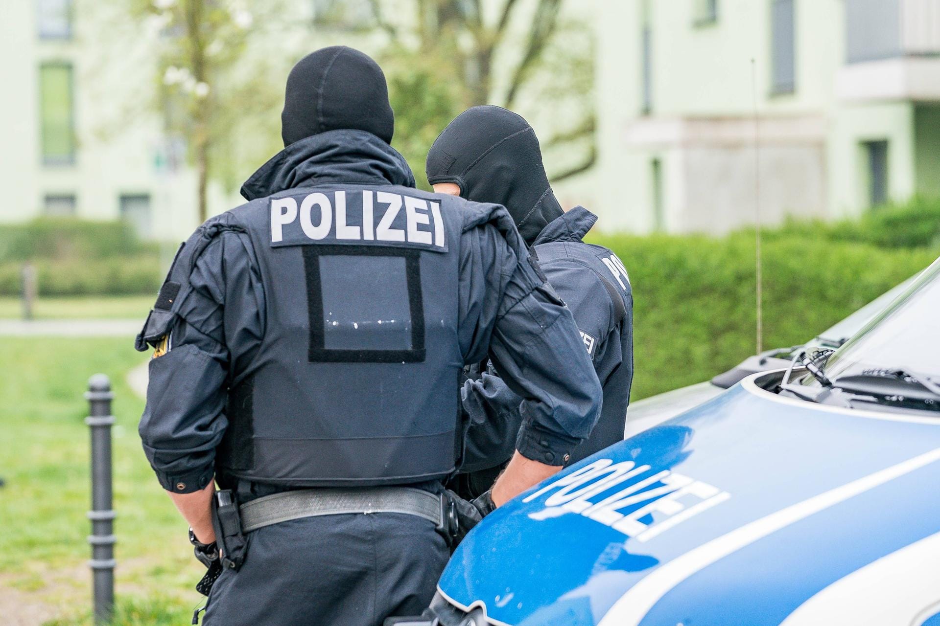 Zwei vermummte Polizisten stehen vor einem Polizeiauto: In Köln und Düsseldorf hat es eine große Razzia gegen mutmaßliche Schleuser gegeben.