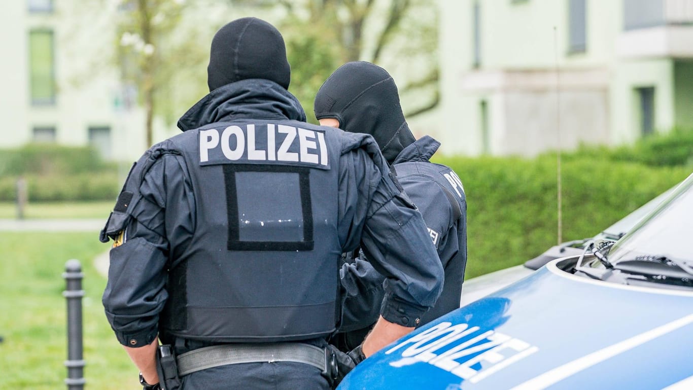 Zwei vermummte Polizisten stehen vor einem Polizeiauto: In Köln und Düsseldorf hat es eine große Razzia gegen mutmaßliche Schleuser gegeben.
