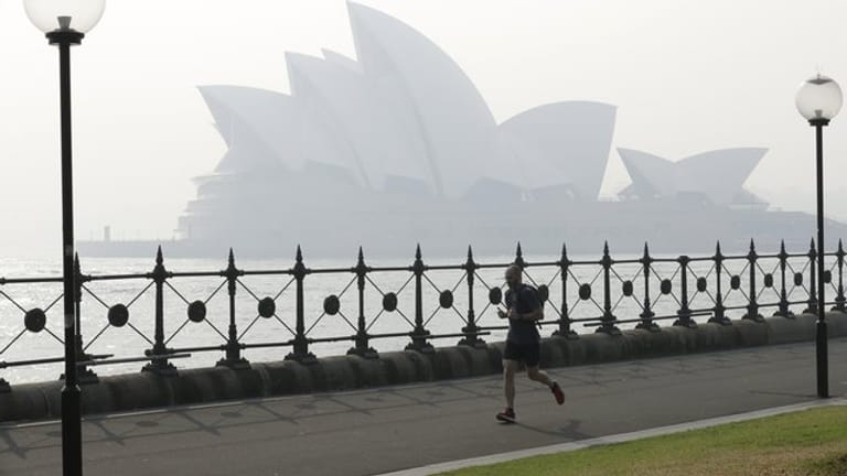 Ein Jogger läuft am Morgen, während Rauchschleier über der Sydney Opera House hängt.
