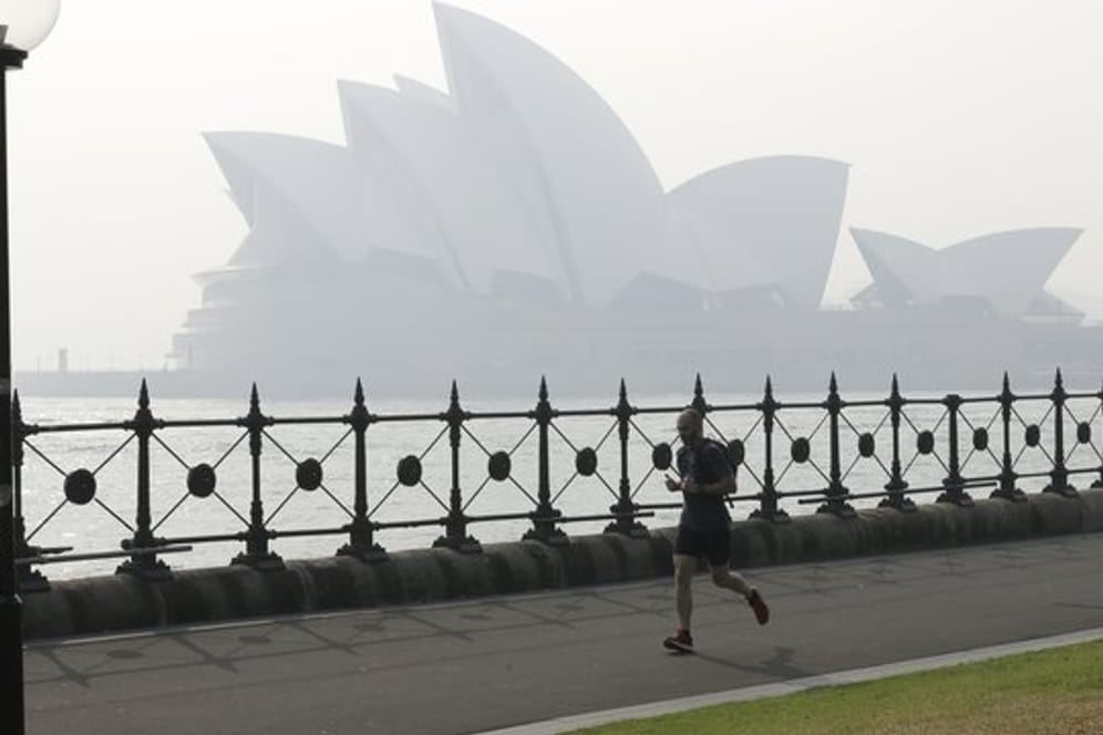 Ein Jogger läuft am Morgen, während Rauchschleier über der Sydney Opera House hängt.