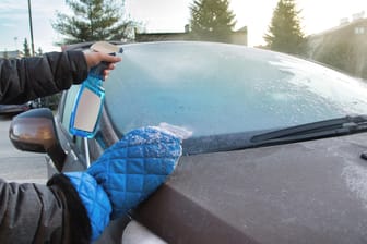 Eine Person sprüht Putzmittel auf eine Autoscheibe: Autofahrer sollten einen frostsicheren Reiniger in der Scheibenwischanlage haben.