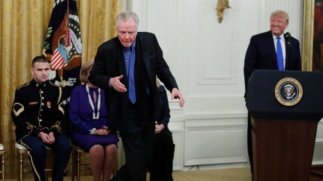 Jon Voight tanzt und Donald Trump lächelt.