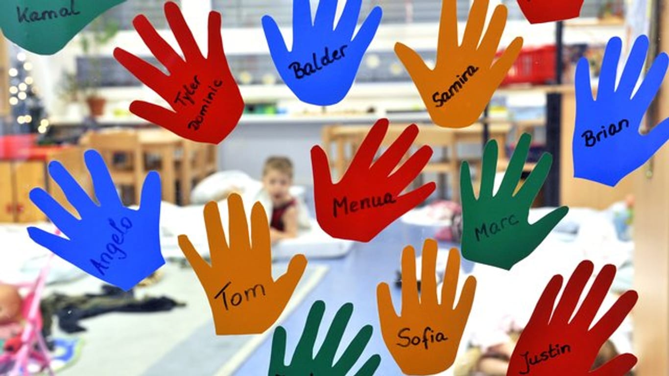 Aus Folien geschnittene Kinderhände hängen mit den jeweiligen Namen an der Eingangstür einer Kindergruppe in einer Tagesstätte.