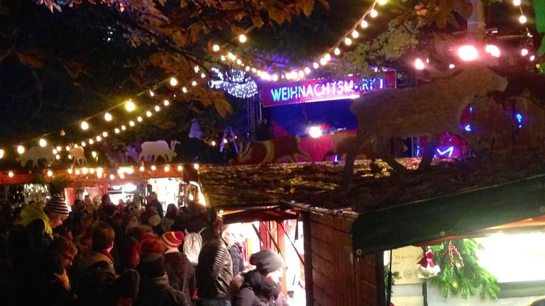Menschen stehen vor beleuchteten Buden: Der Weihnachtsmarkt im Stadtgarten ist trendig und beliebt.