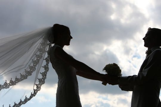 Die Silhouette eines frisch vermählten Hochzeitspaares zeichnet sich im Gegenlicht ab.