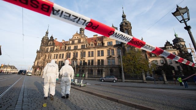 Zwei Mitarbeiter der Spurensicherung stehen vor dem Residenzschloss mit dem Grünen Gewölbe hinter einem Absperrband.