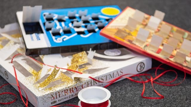 Leere Adventskalender liegen zusammen mit einer Rolle Geschenkband auf dem Boden. Leere Adventskalender liegen zusammen mit einer Rolle Geschenkband auf dem Boden.