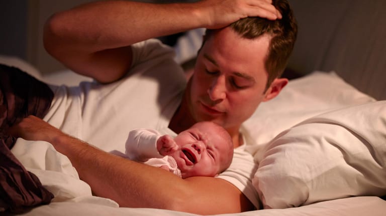 Ein Vater mit einem weinenden Säugling im Arm: Viele Eltern verzweifeln, wenn ihr Kind einfach nicht einschlafen will.