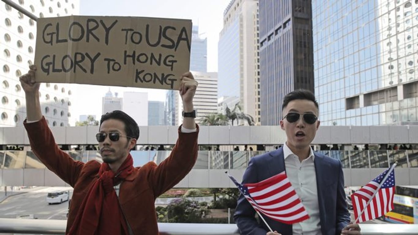 Demonstranten halten amerikanische Flaggen und ein Plakat mit der Aufschrift "Glory to USA, Glory to Hong Kong" ("Ruhm für die USA, Ruhm für Hong Kong") hoch.