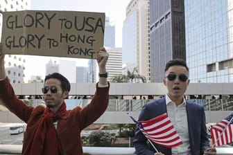 Demonstranten halten amerikanische Flaggen und ein Plakat mit der Aufschrift "Glory to USA, Glory to Hong Kong" ("Ruhm für die USA, Ruhm für Hong Kong") hoch.